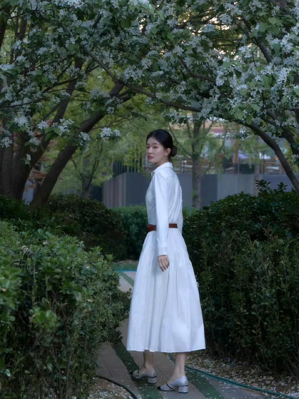 走在白色樱花树林下的她，穿着一身白色连衣长裙，尽显她优雅淑女范的气质！90后的她