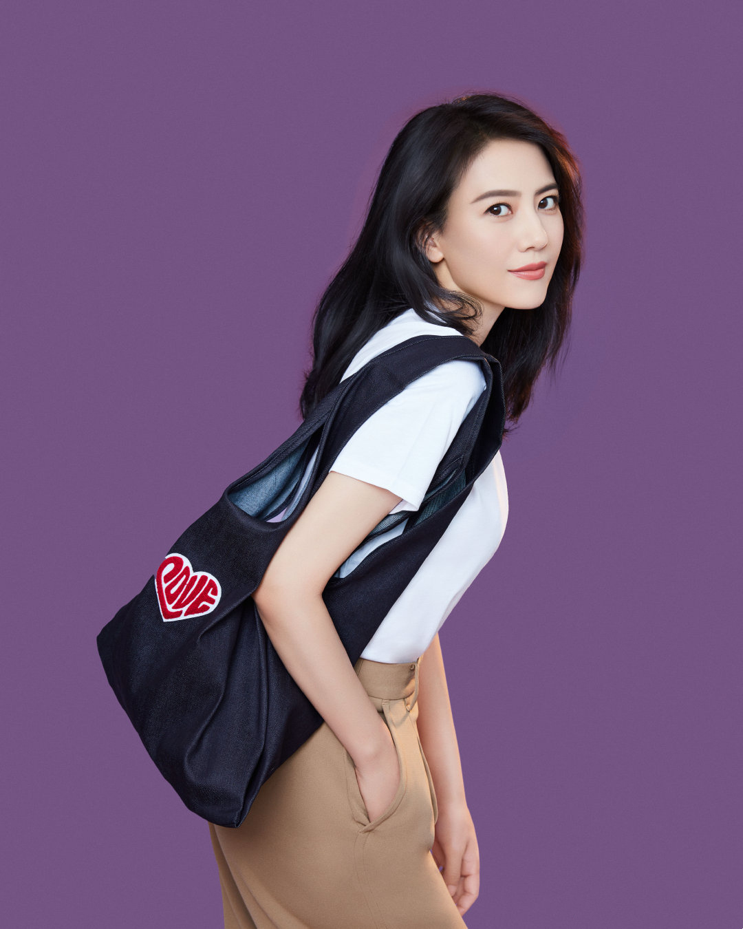 侧身倚立，黑包红心的点缀亮眼，素色衣着衬出清丽五官，一转头的瞬间，温婉中透着灵动