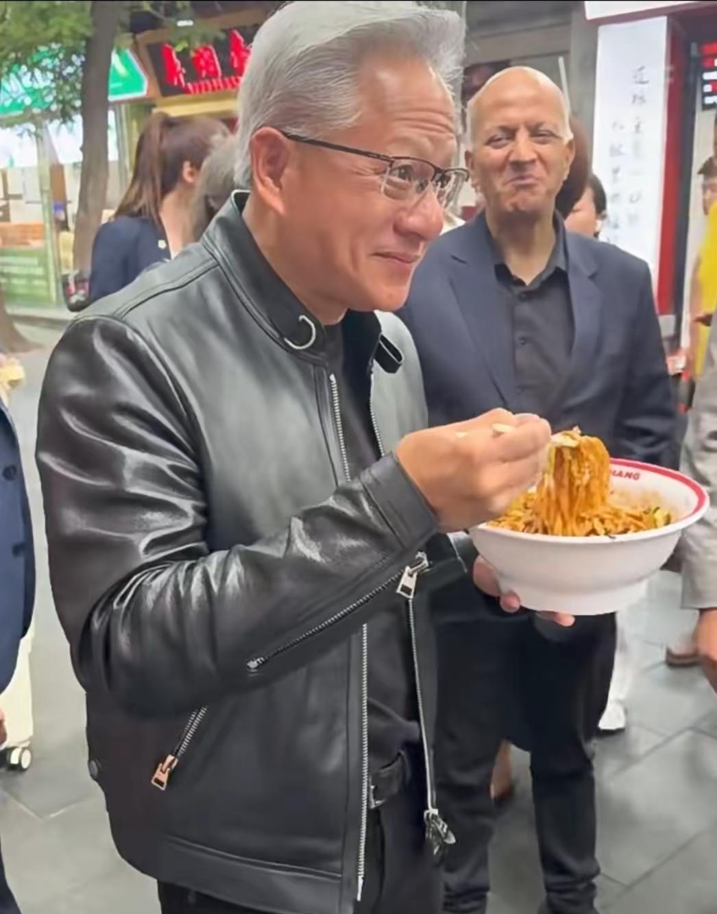 今儿中午，有网友在北京南锣鼓巷撞见黄仁勋了。这位AI大佬穿着标志性皮衣，端着炸酱