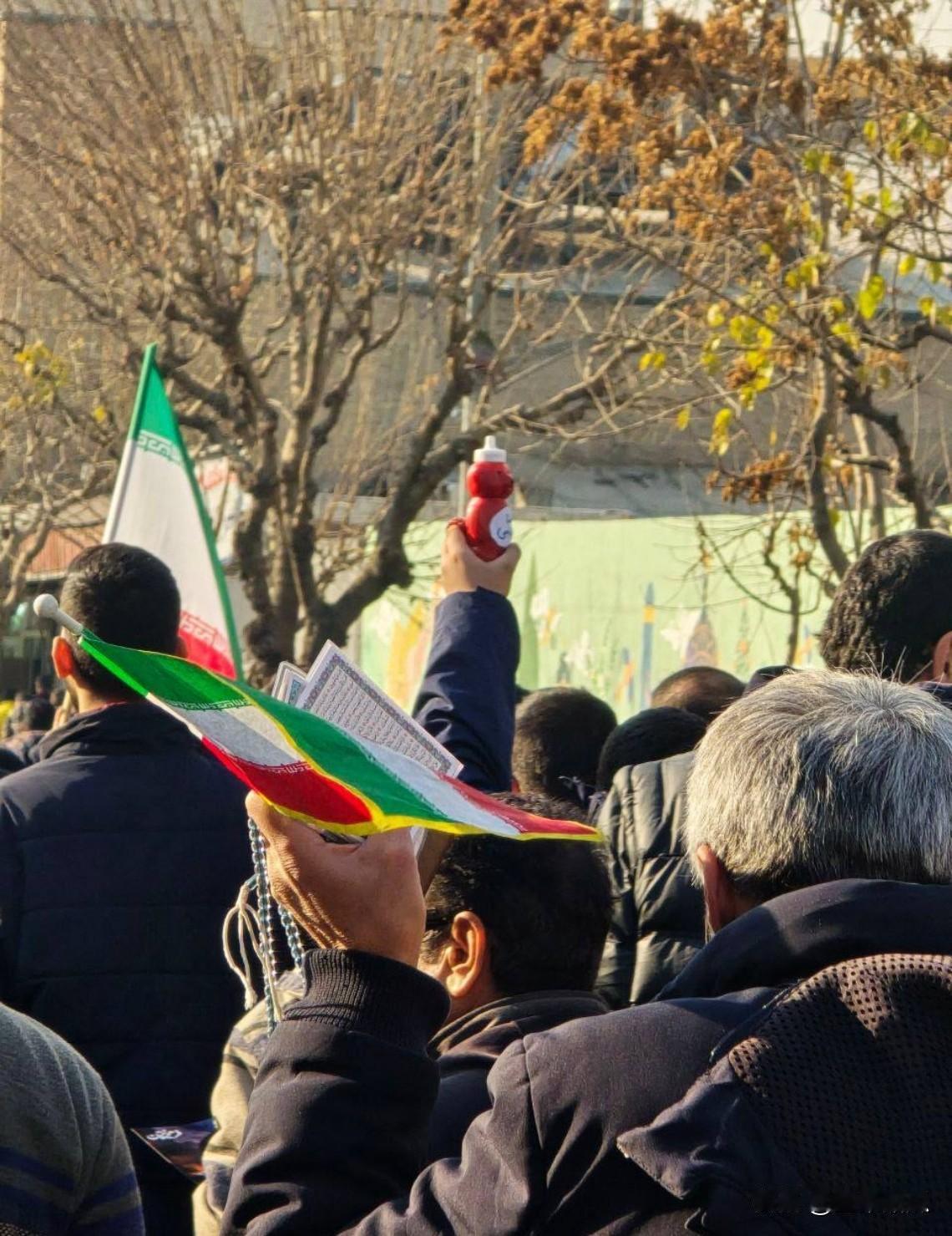 伊朗某地游行，一人举起《古兰经》，另一人举起一瓶酷似礼萨·巴列维总统脸的番茄酱。