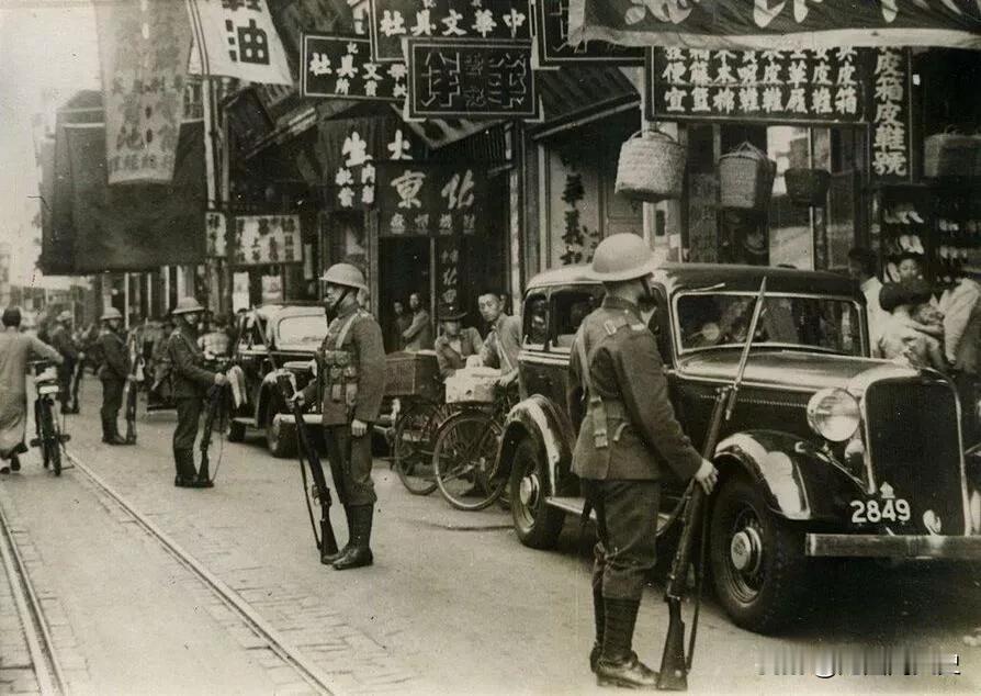 上世纪三十年代的老上海，几名全副武装的英国士兵正在街头站岗，路边还停着两辆小汽车
