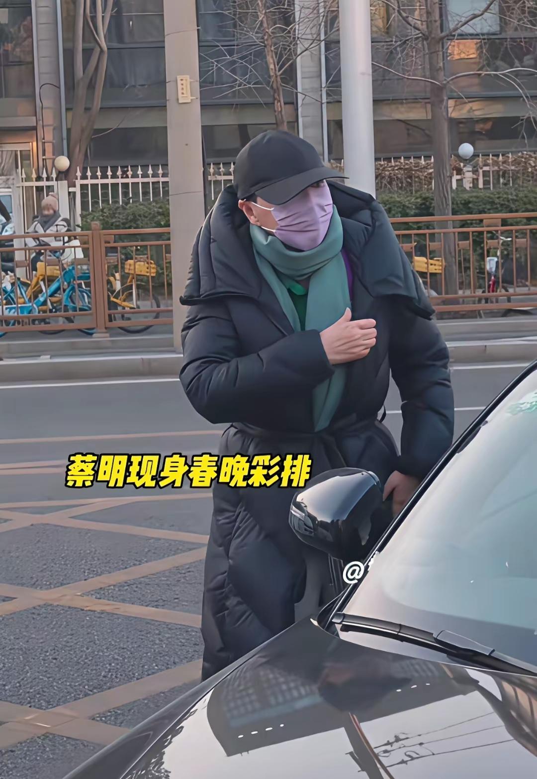 蔡明春晚彩排路透照，穿黑色长款羽绒服，搭配橘色围巾，头戴黑色棒球帽，裹得严严实实