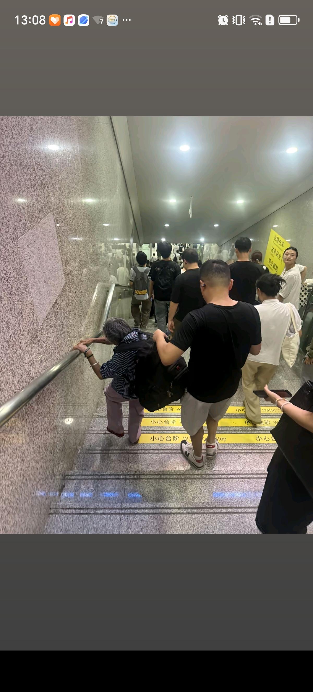 火车站里，前面的老太太背着超大号的黑色双肩包小心的扶着楼梯扶手一步步往下走，后面