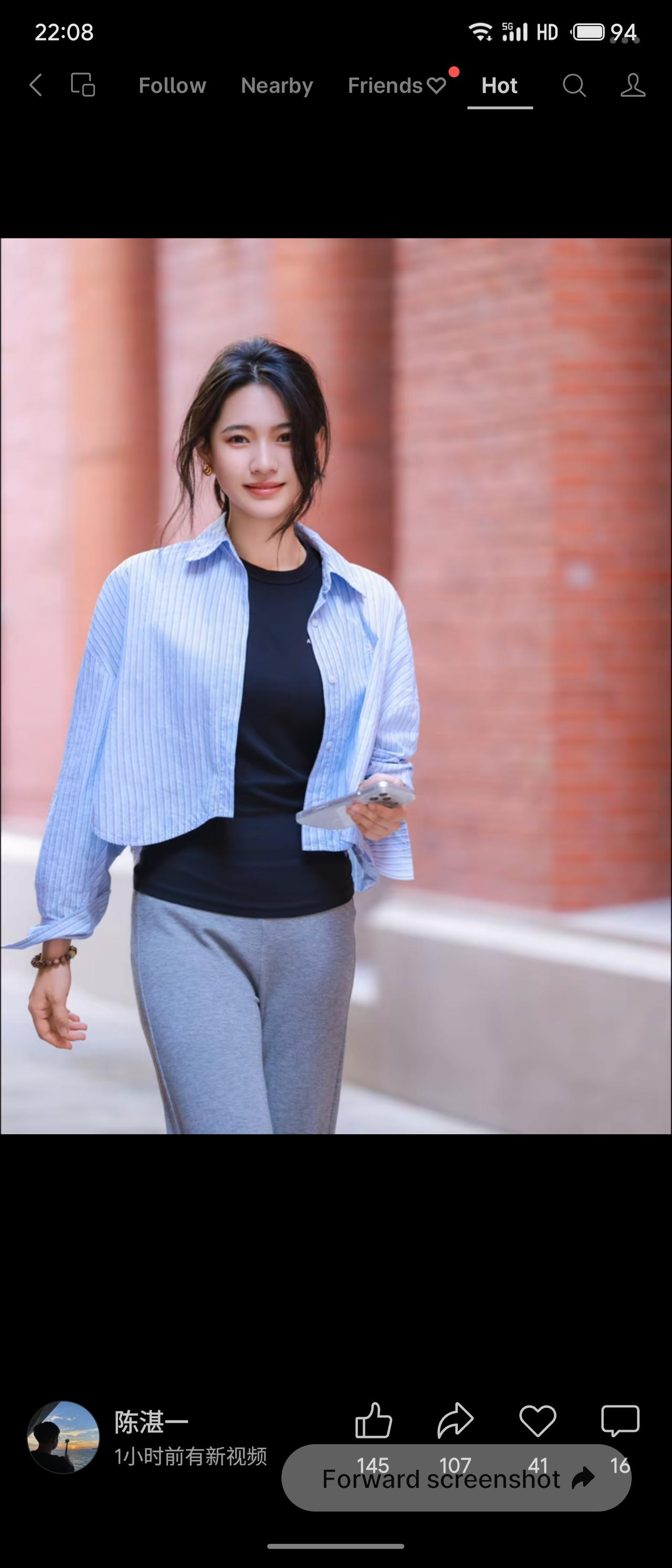 红砖街巷间，女生内搭黑色修身短袖，外搭短款蓝条纹衬衫，搭配灰色垂感休闲长裤。发丝