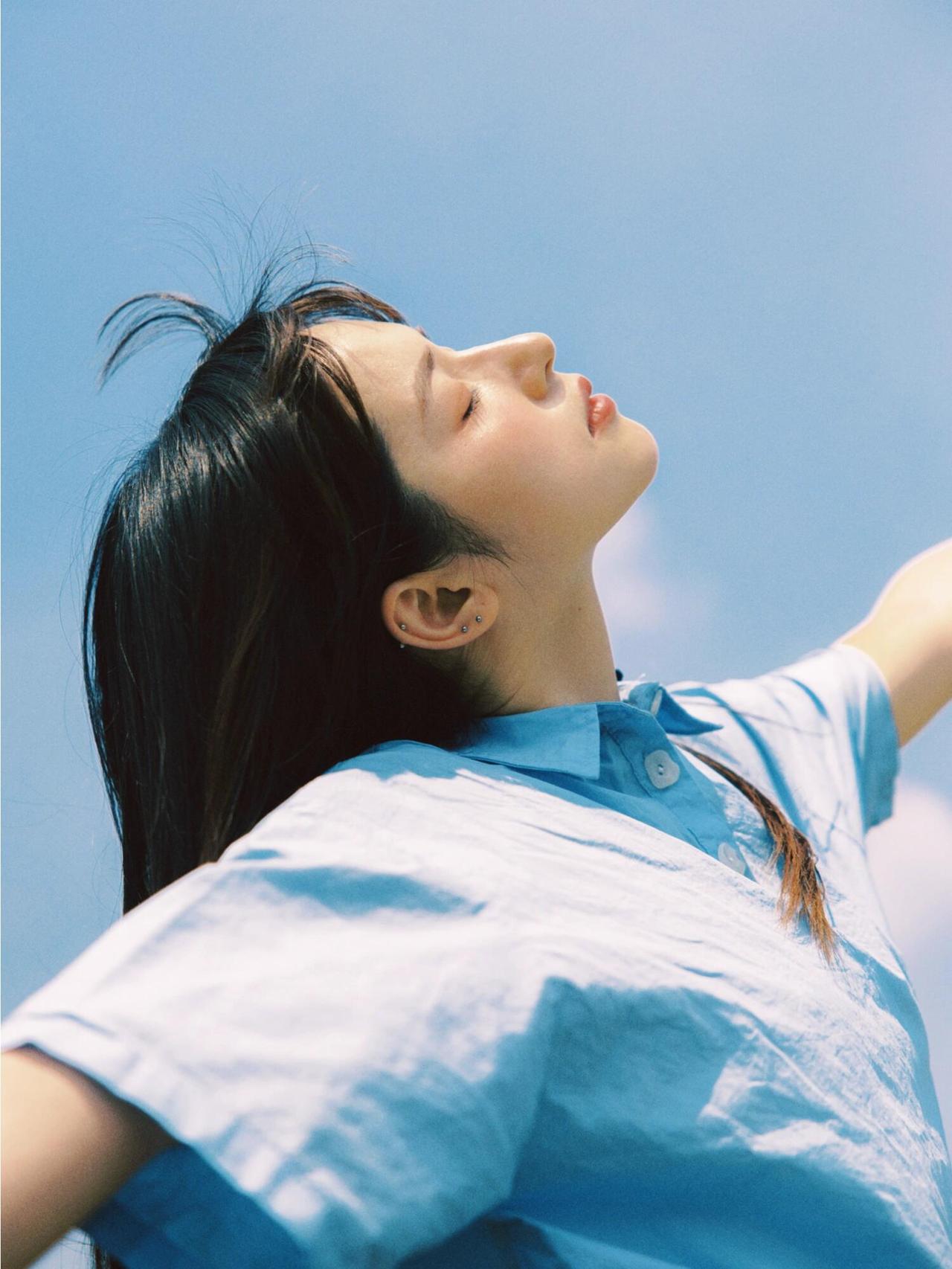 看一下学生装的少女拍摄，画面里，少女在草地上跃起，伸手向云朵。蓝天为幕，草地作台