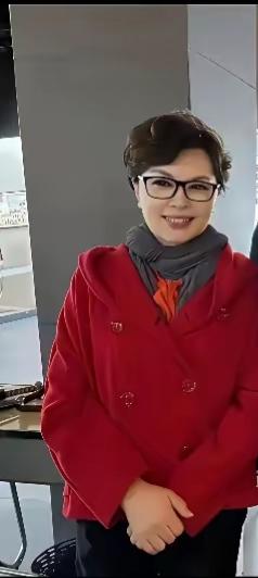 这位女士穿着红色外套，面带微笑。看着很面熟，她是那位中央主持人吗？大家仔细看看是