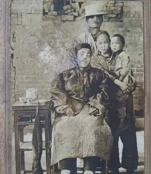 这是一张全家福照片，照片中坐在椅子上的男子眼睛紧闭，身体僵硬，头歪向一边，此刻他