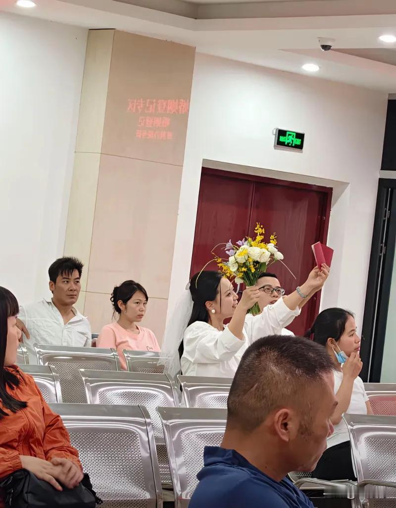这张在民政局婚姻登记处拍下的照片，道尽了婚姻最扎心的两面：一对新人捧着鲜花、高举