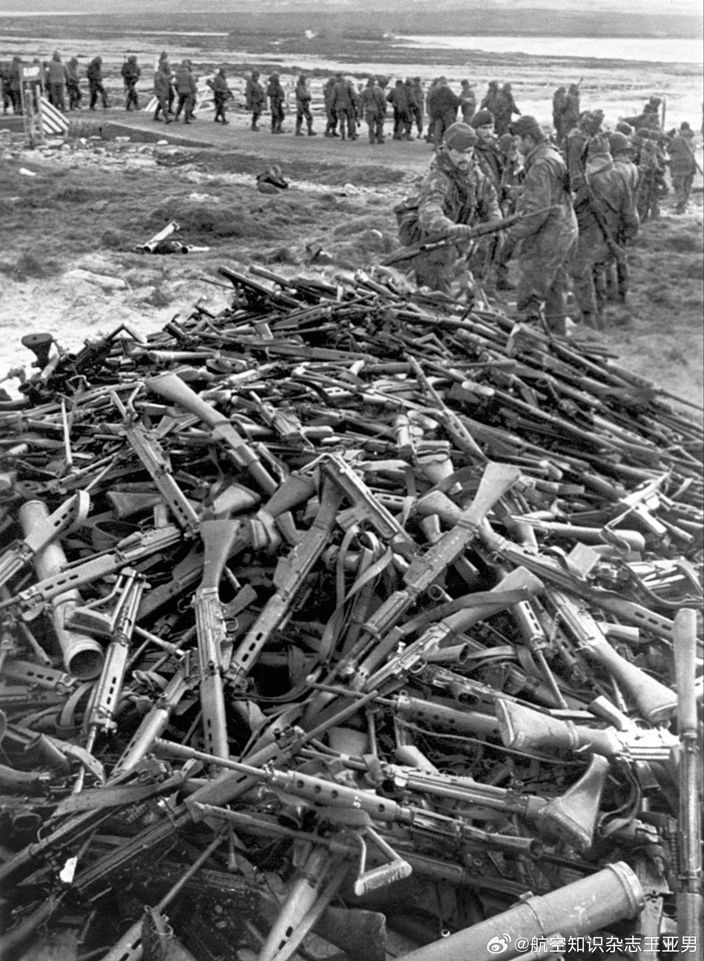 阿根廷士兵排成一队，挨个把自己的武器散乱堆放在一起，移交给英国海军陆战队，这一幕