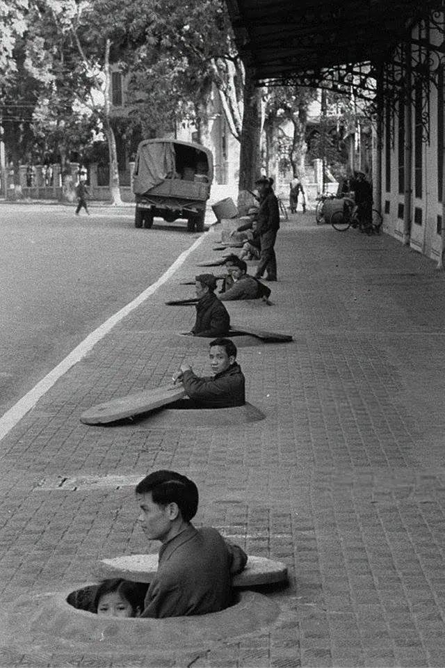 1967年，北越河内，空袭警报响起，居民们躲在齐胸深的人行道防空洞里等待解除警报