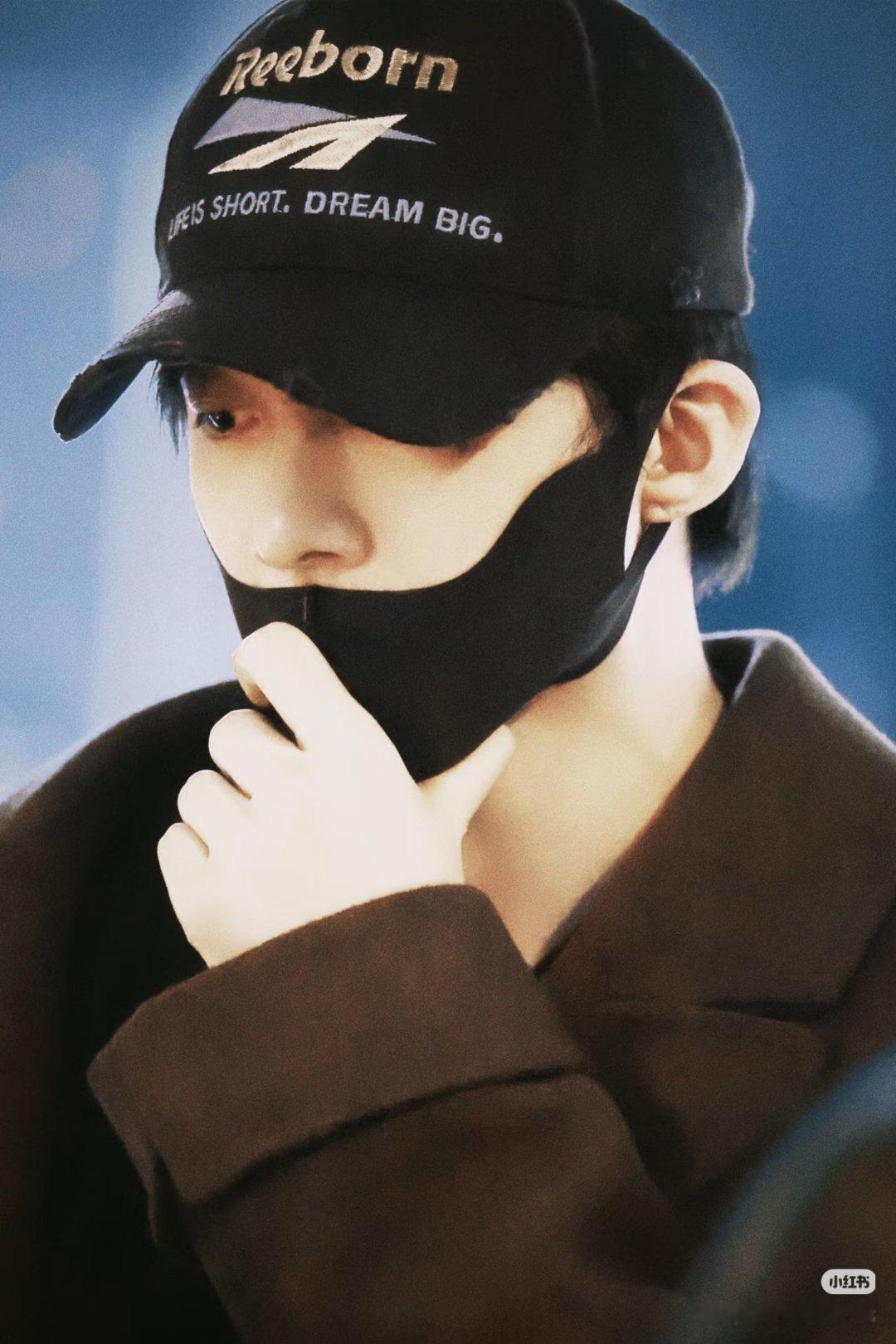 焦糖棕大衣搭配黑色棒球帽，抬手调整口罩的瞬间，侧颜线条利落又精致；蓝调光影里轻触