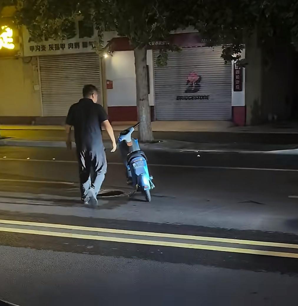 一辆共享电瓶车随意丢在车道上，男子好心上前想要把挡路的电动车挪走，注意力都放在车