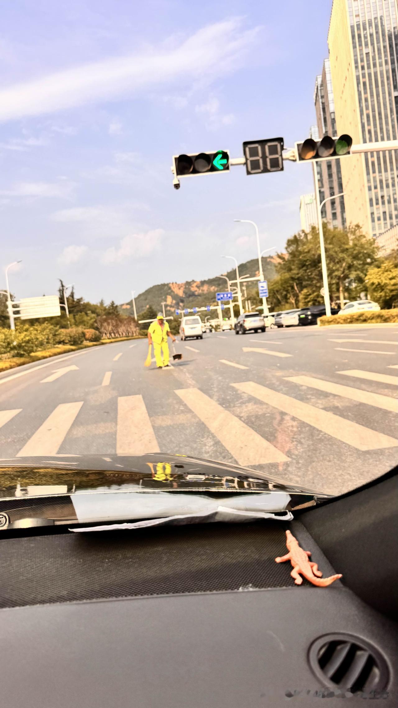青岛株洲路一路口，车辆川流不息。刚过路口，忽见正前方一环卫老者正在车流中埋头扫马