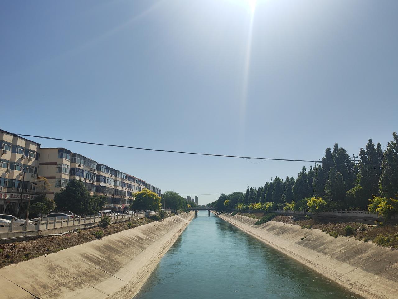 晒图笔记大赛早晨，朝阳下的石津渠，天蓝水绿，两岸绿树浓荫，北侧是一排排整齐的楼房