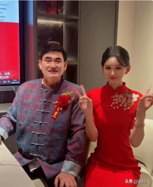 朱之文胸前佩戴红花，身穿中式唐装，参加活动时与女主持人的一张合影。网友调侃：不仔
