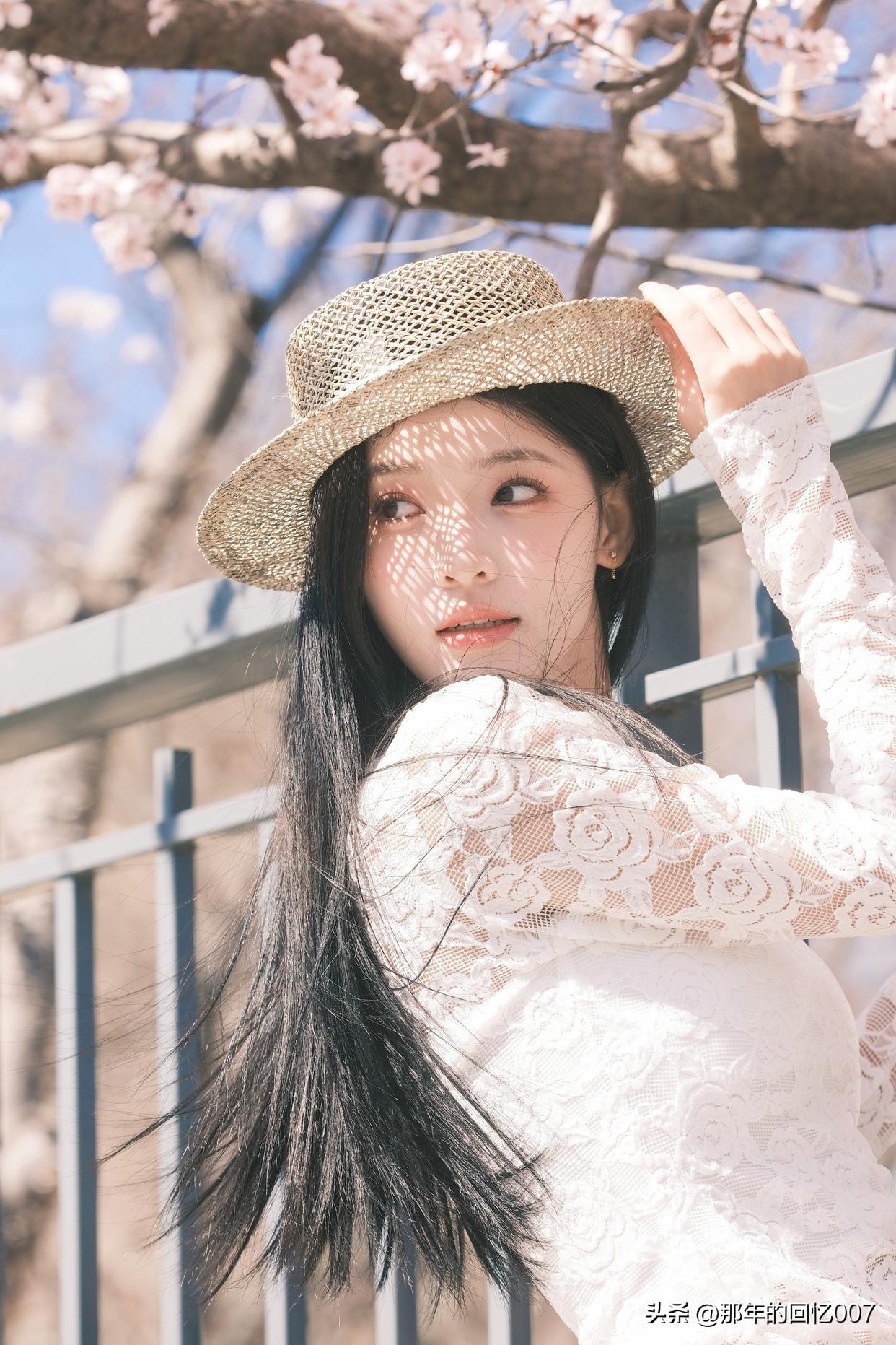 春日樱花烂漫，仿佛是一场粉色的梦境。一位少女静静地站在樱花树下，轻柔地抚了抚帽檐