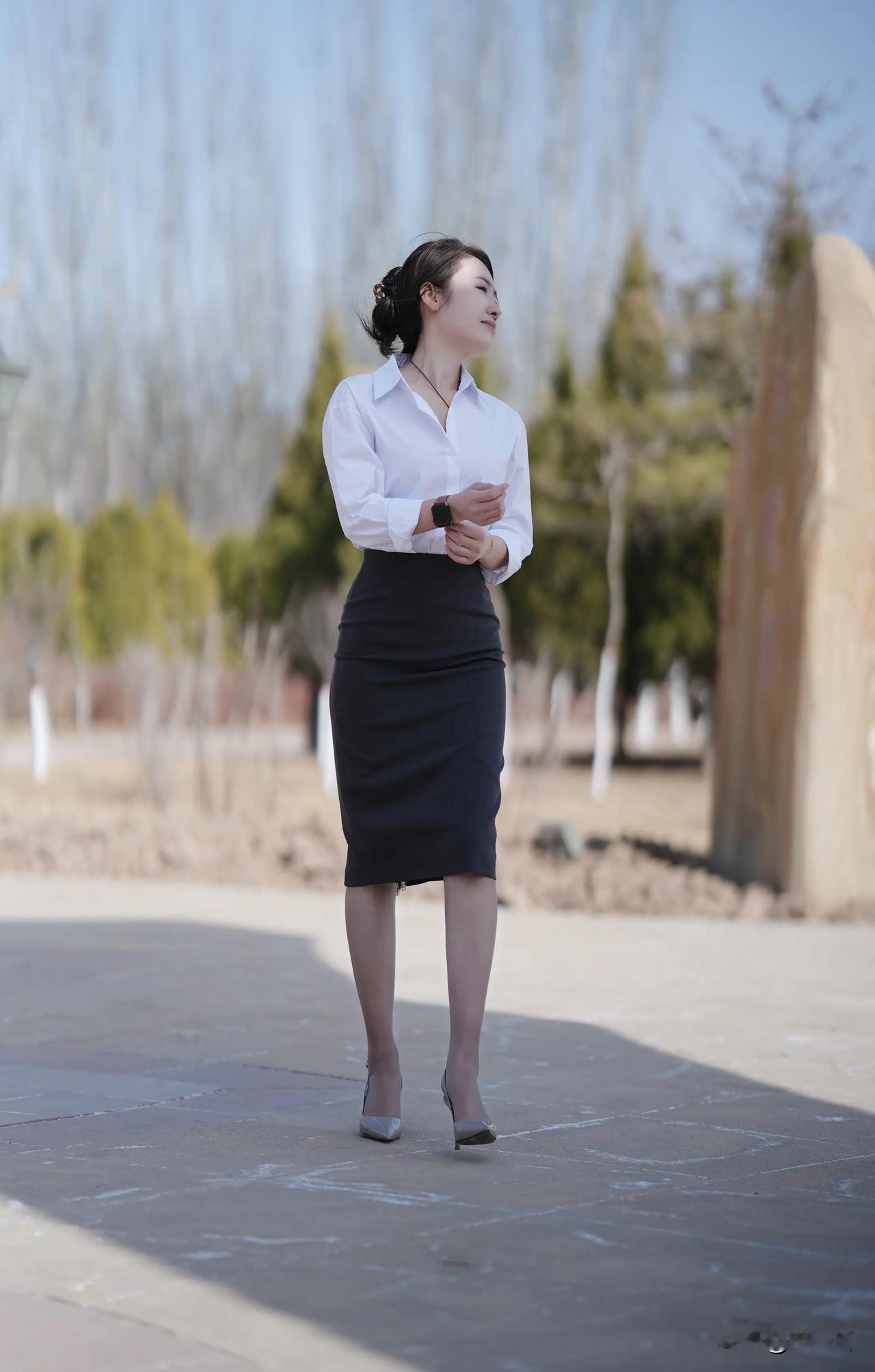一个穿白衬衫和黑裙子的女生在户外。