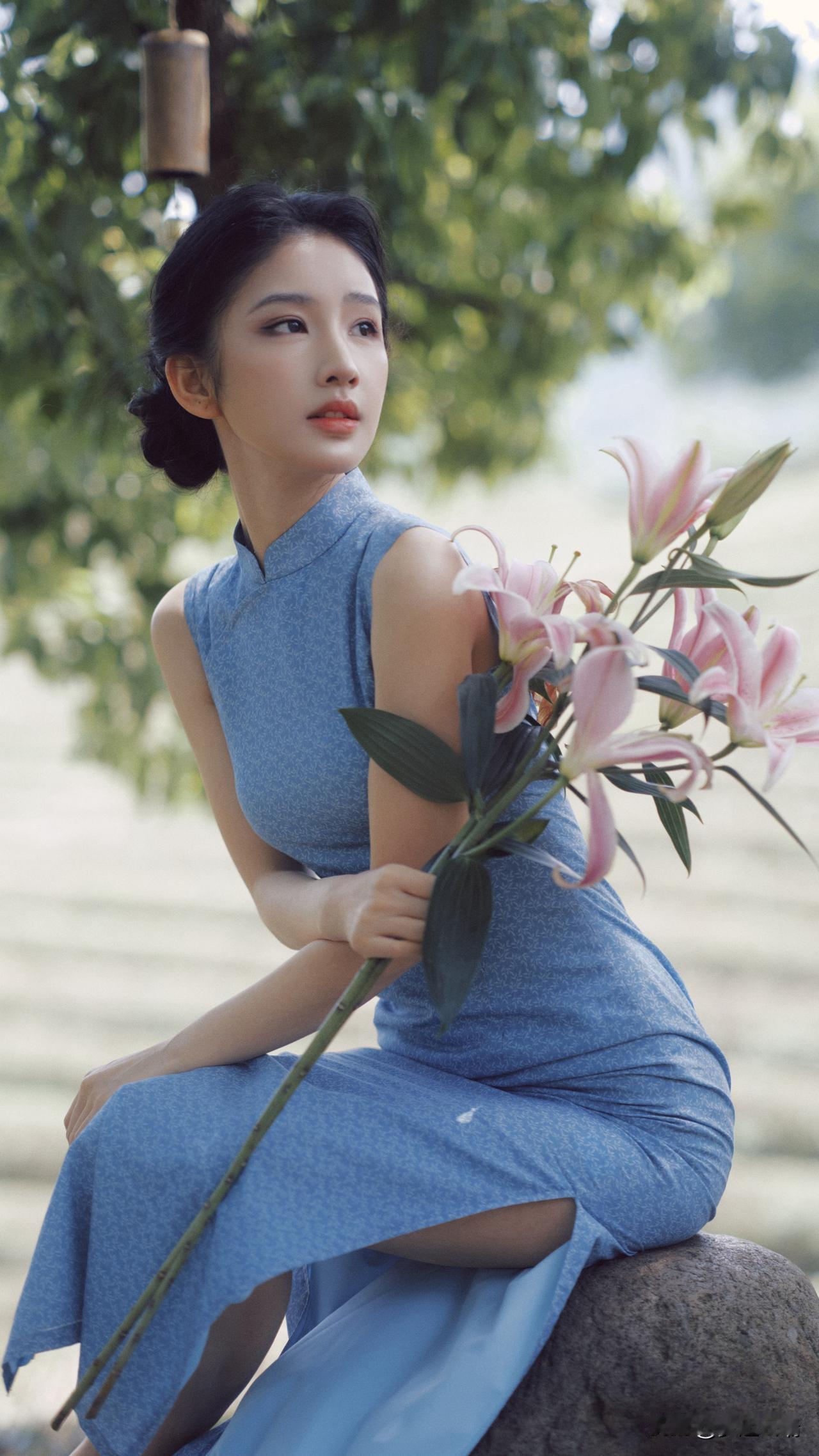 优雅蓝裙少女，手捧粉色百合，静坐绿意盎然中。