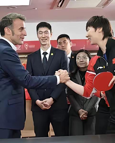 马克龙紧握着王曼玉的手:乒乓球我是打不过你的，但是扳手腕，我就不信也扳不过你，因