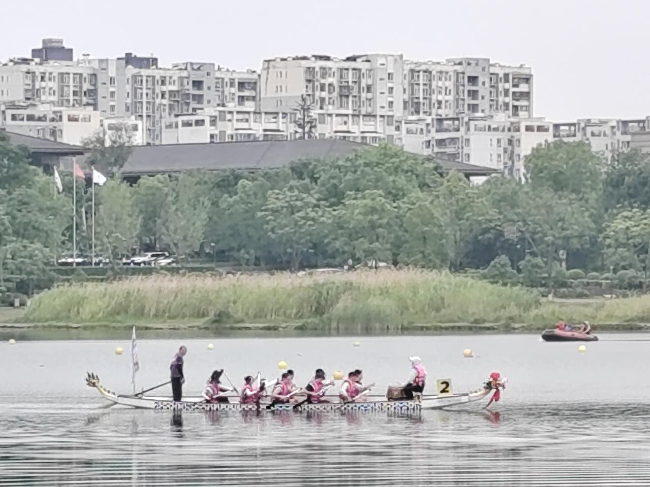 锦城湖湖面水波轻漾，一场热闹的龙舟赛事正在上演。几艘龙舟并列水面，队员身着统一红