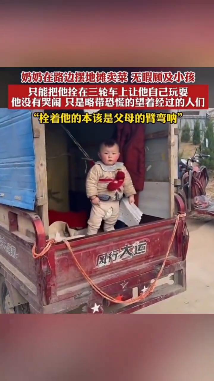 奶奶在路边摆地摊卖菜无暇顾及小孩，只能把他拴在三轮车上让他自己玩耍。他没有哭闹只