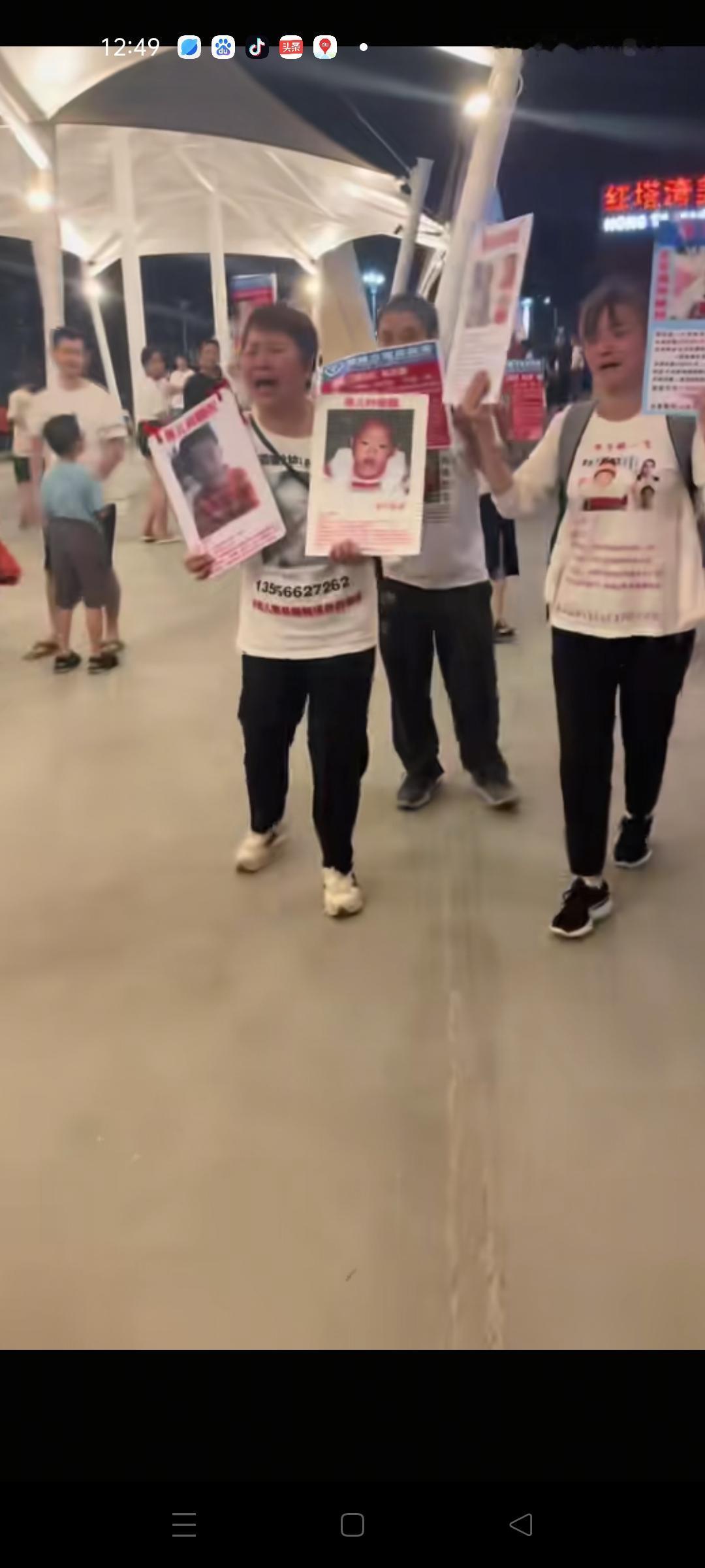 叶锐聪妈妈手机举着寻亲牌子，身穿印着孩子照片的寻亲服，走在大街上哭喊着寻求大家帮