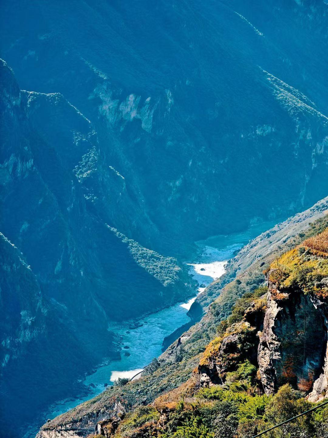 虎跳峡，身旁是陡峭的山壁，远处云雾缭绕在山峰之间，江水在峡谷中奔腾，在这虎跳峡的