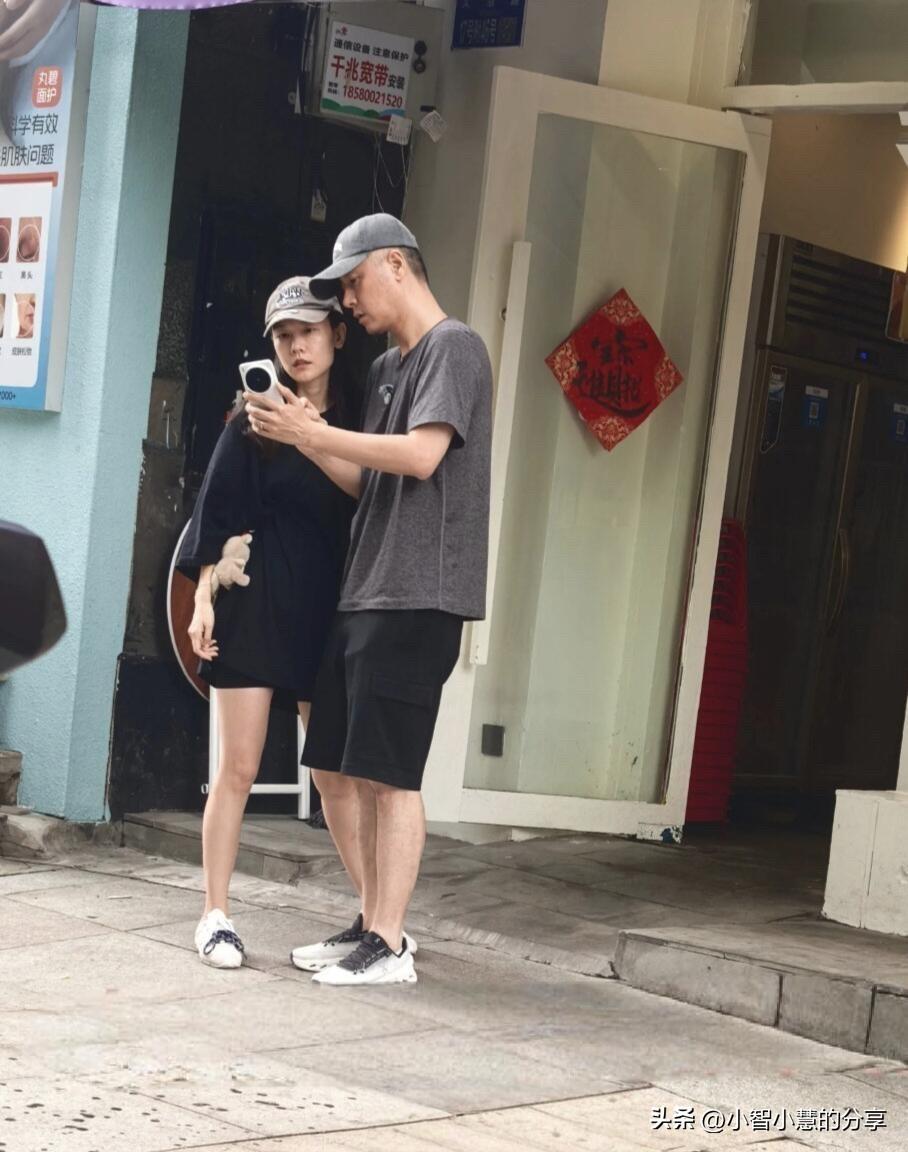46岁任重和老婆戴着帽子，两个人穿搭简约比较休闲，在外面一起逛街，他指着手机上的