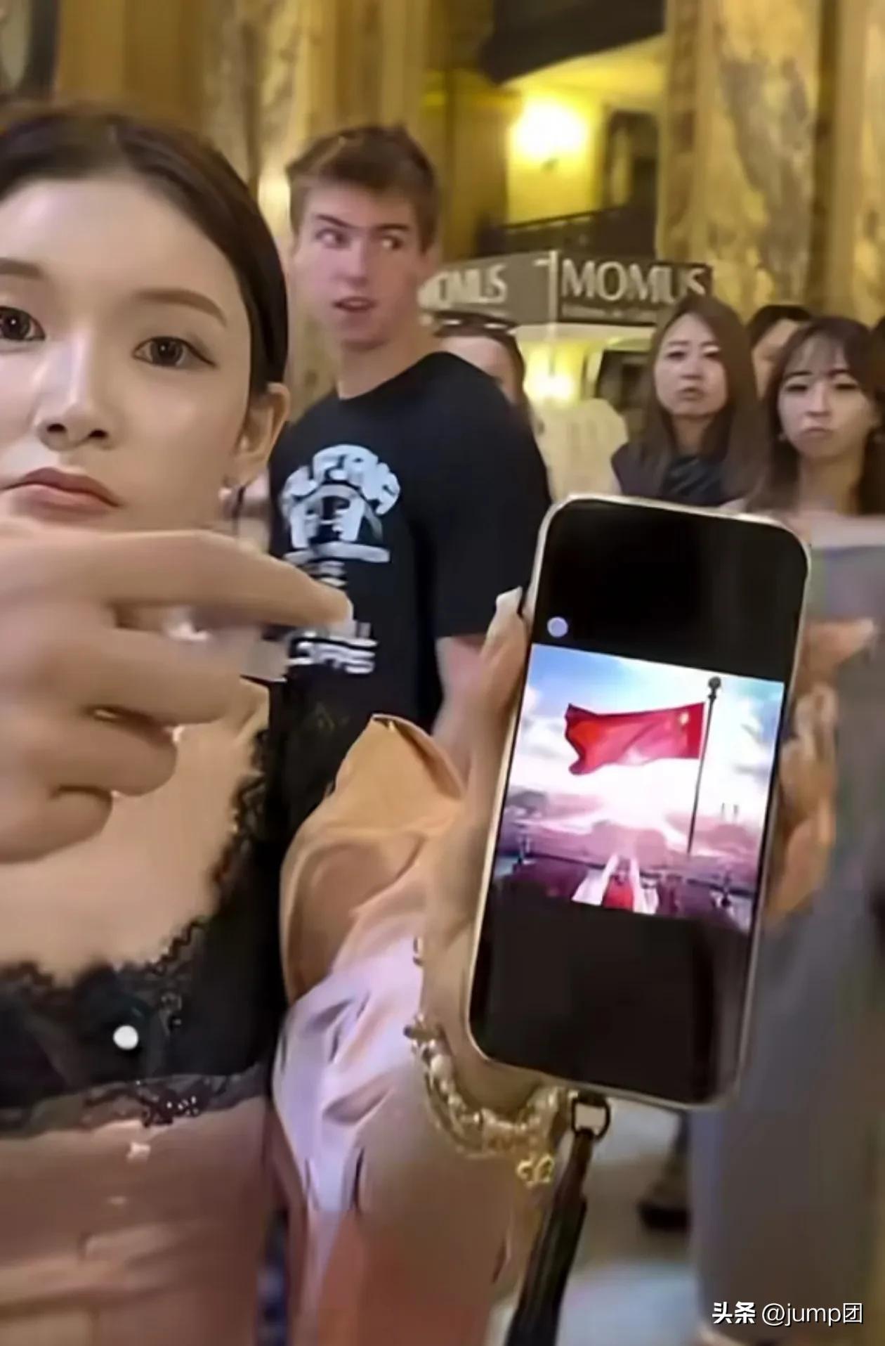 巴黎歌剧院门口一个聋哑女人举着手机屏幕上的五星红旗冲着围观的老外嘶哑地喊叫，她男