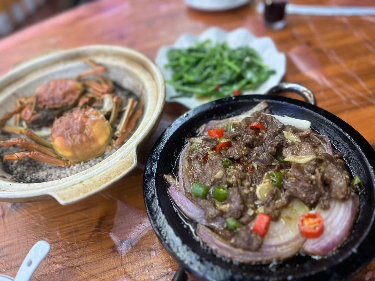 桌上有盘螃蟹和炒牛肉，一碟青菜很有食欲。