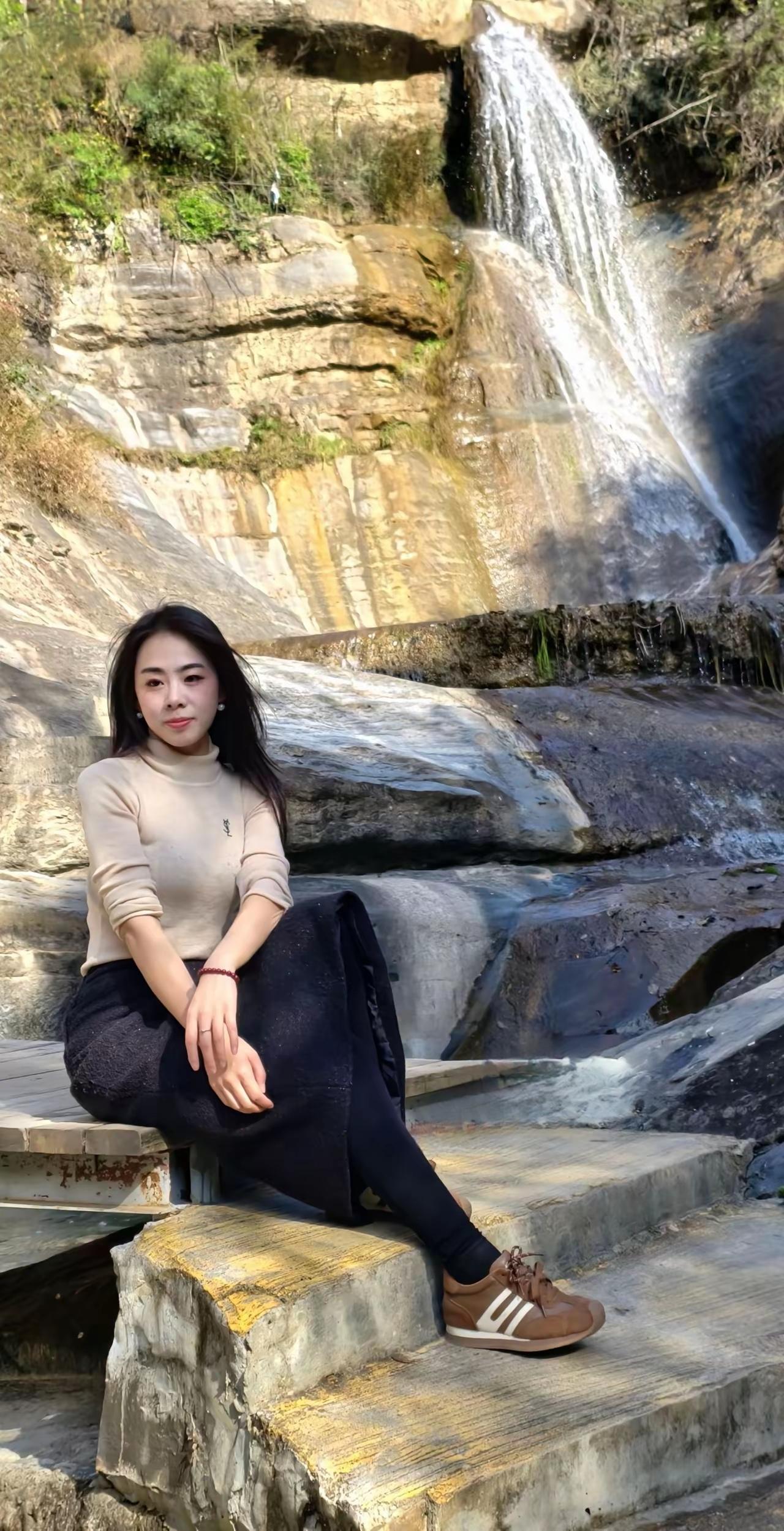 女孩坐在瀑布前的台阶上晒太阳。