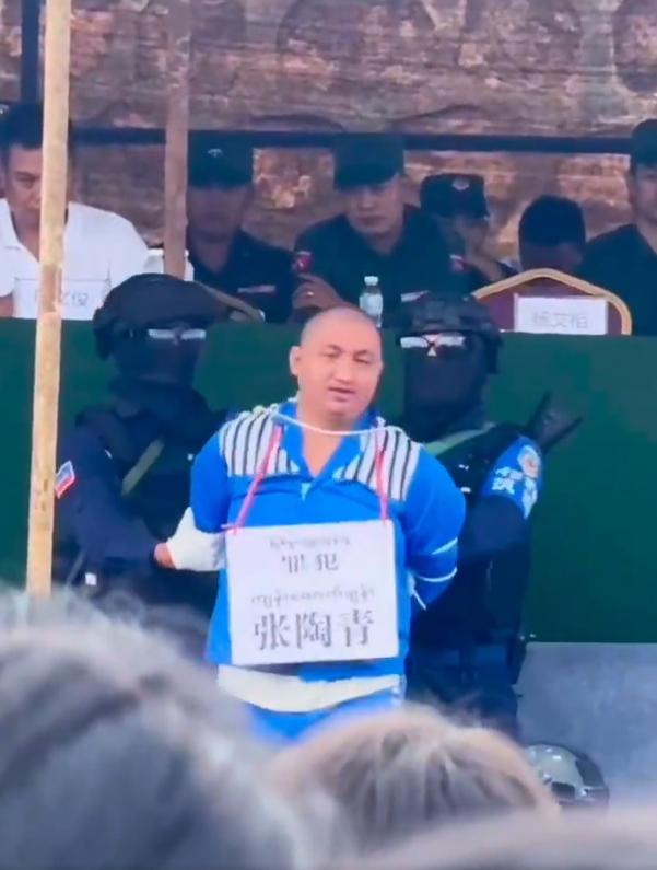 一段缅甸果敢公开宣判活动的视频，画面中多名身穿蓝色运动服的囚犯颈挂写有中文罪名（