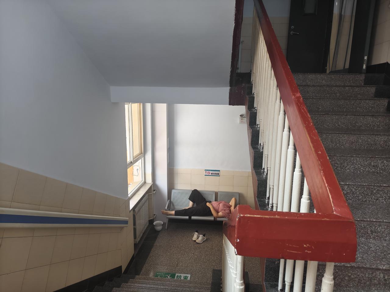 在运城市盐湖区人民医院的走廊，一位中年妇女躺在走廊的座椅上休息，任凭行人走动，她