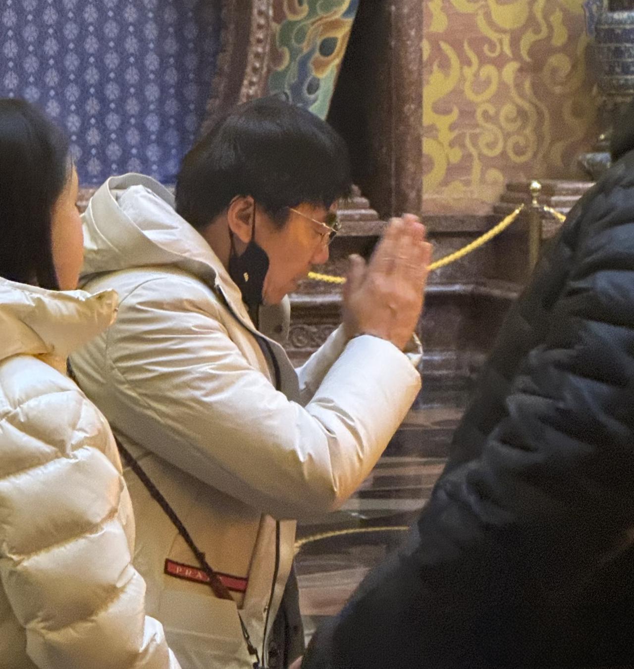 61岁范明和家人现身南京牛首山祈福，他穿着一件白色羽绒大衣，对着庙里的神像双手合
