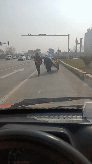 马路上拍到两位老人拉着一车木头从车前经过。
老人佝偻着身子十分吃力的拉着板车，在