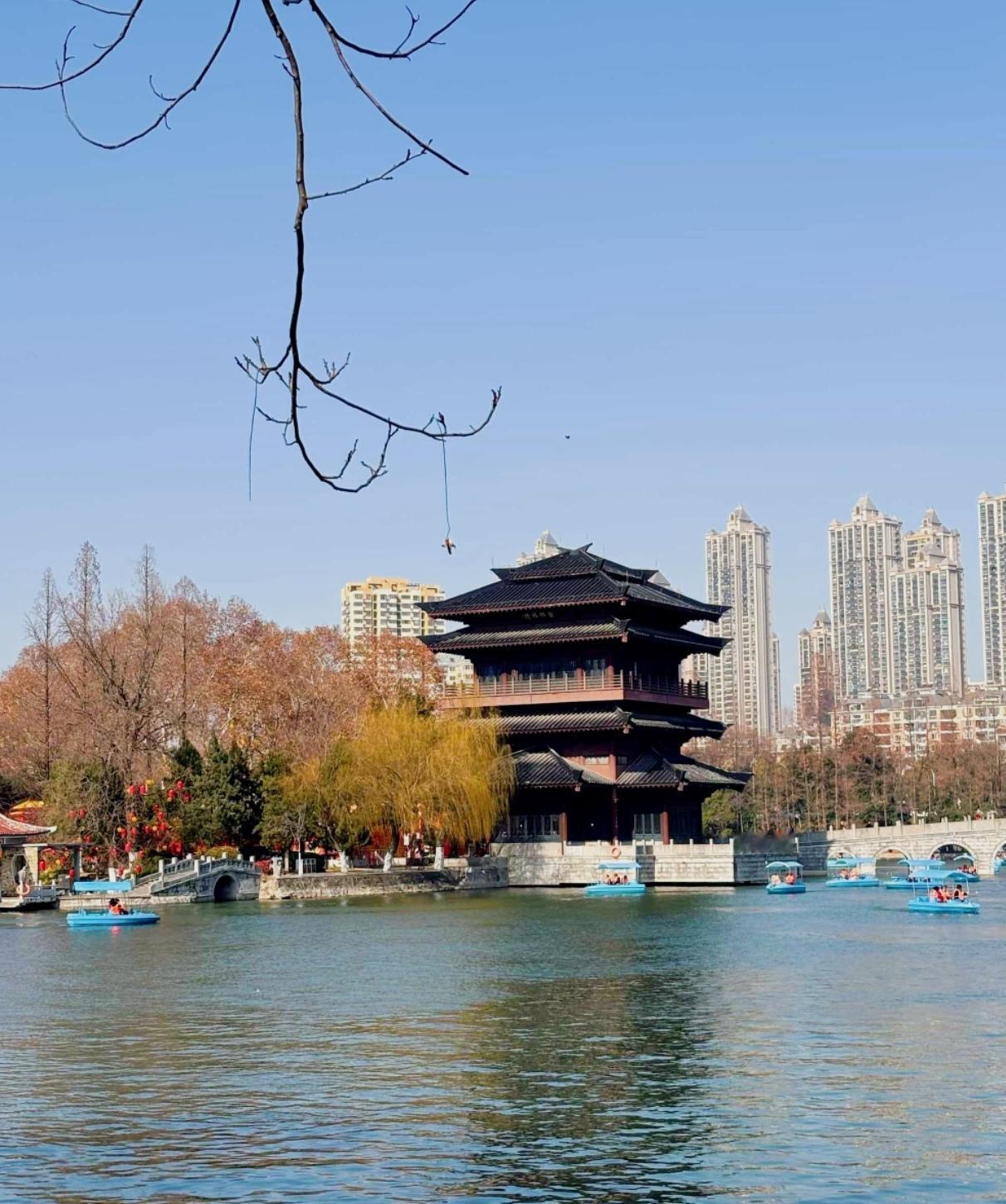 湖水澄澈萦绕翠岛，亭榭枕波而立，飞檐揽住流云晚风。依依垂柳轻吻湖面，曲径回廊藏尽