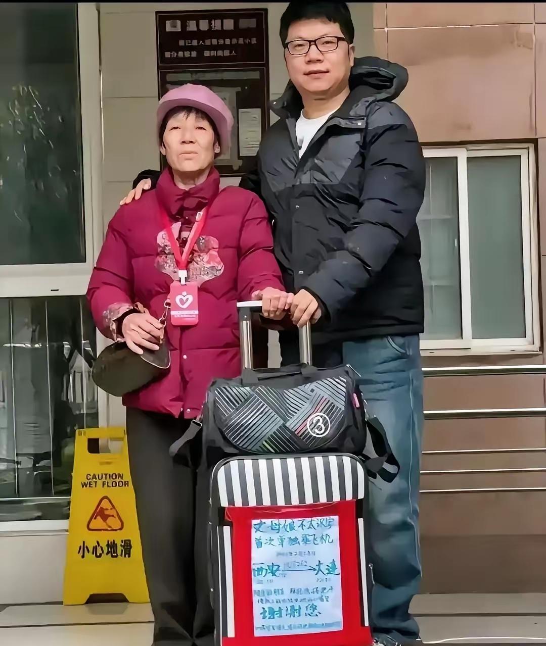 机场里，小伙子给丈母娘送行，老人的行李箱上贴着一张纯手工写的大海报，上面写着:“