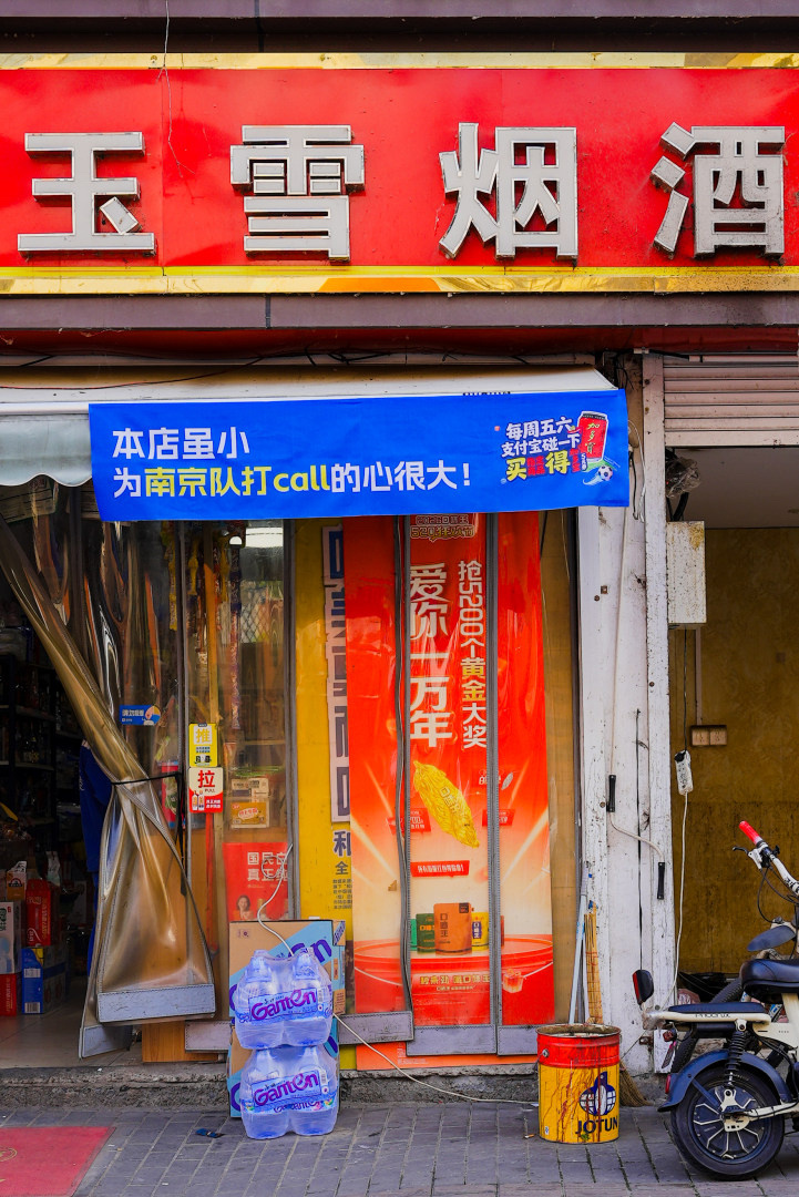 百店发支付宝助威袋为南京队加油走在南京街头，不少便利店都挂起了助威横幅，氛围感直