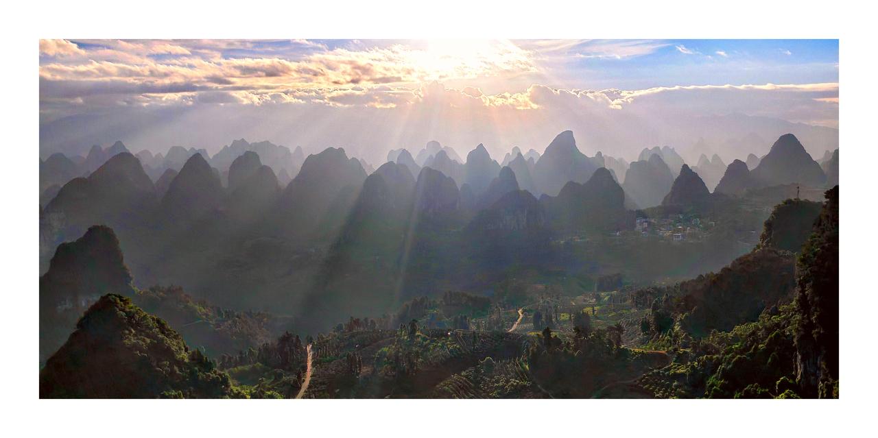 云雾缭绕的喀斯特山峰，阳光洒下，宛如仙境。