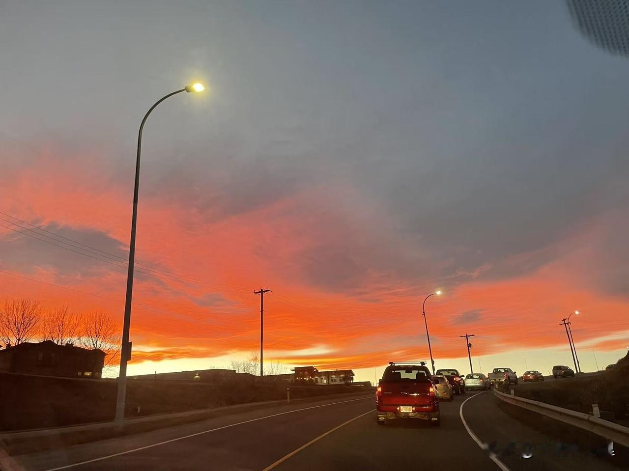 天边燃起一片胭脂火，铺成流金的海。
路灯先亮，像夜色递来的温柔。
车影缓行，驶进