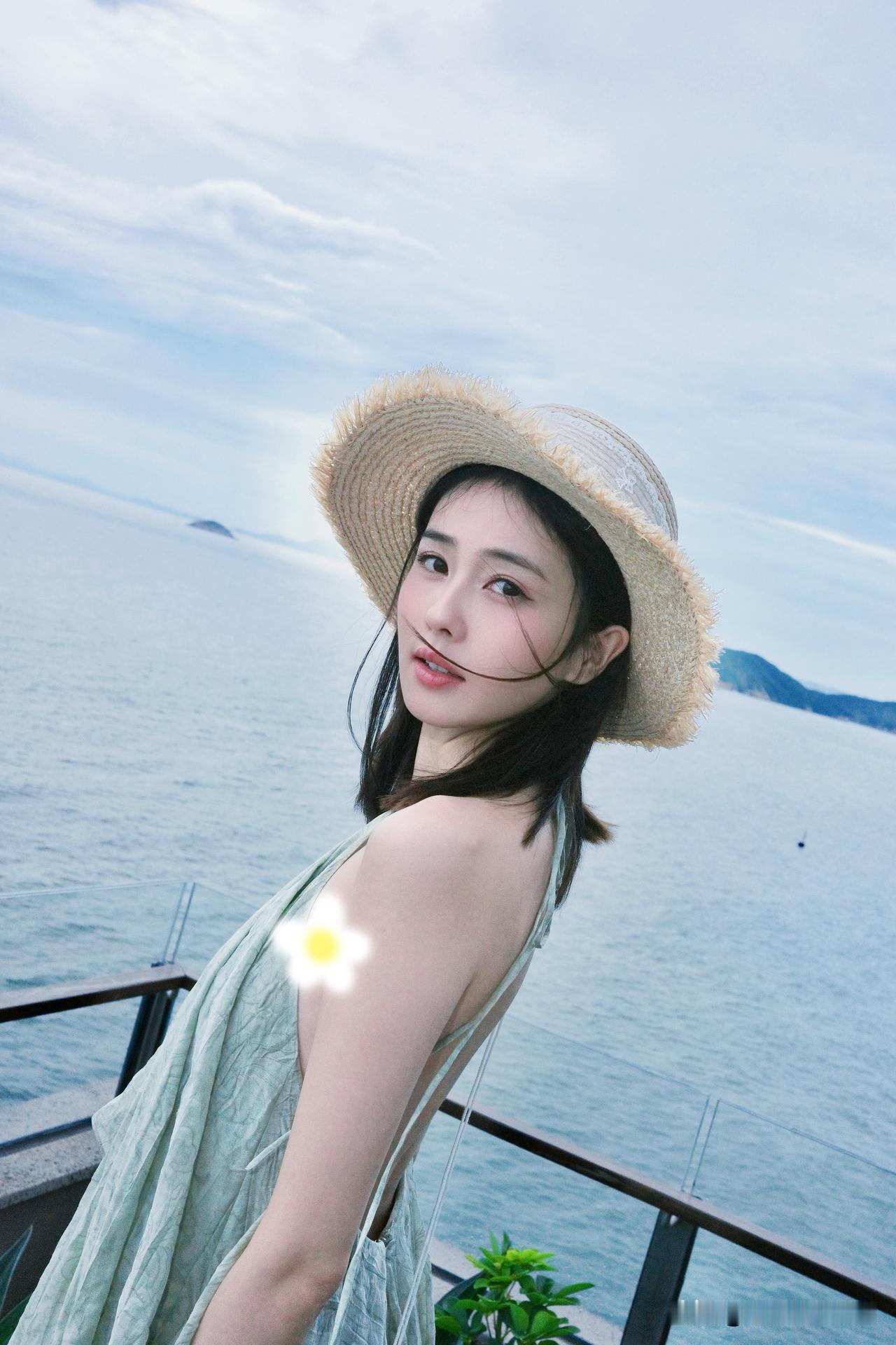 31岁白鹿分享海边度假plog，她身穿浅绿色挂脖吊带裙，头戴草帽，脸色红润，整个