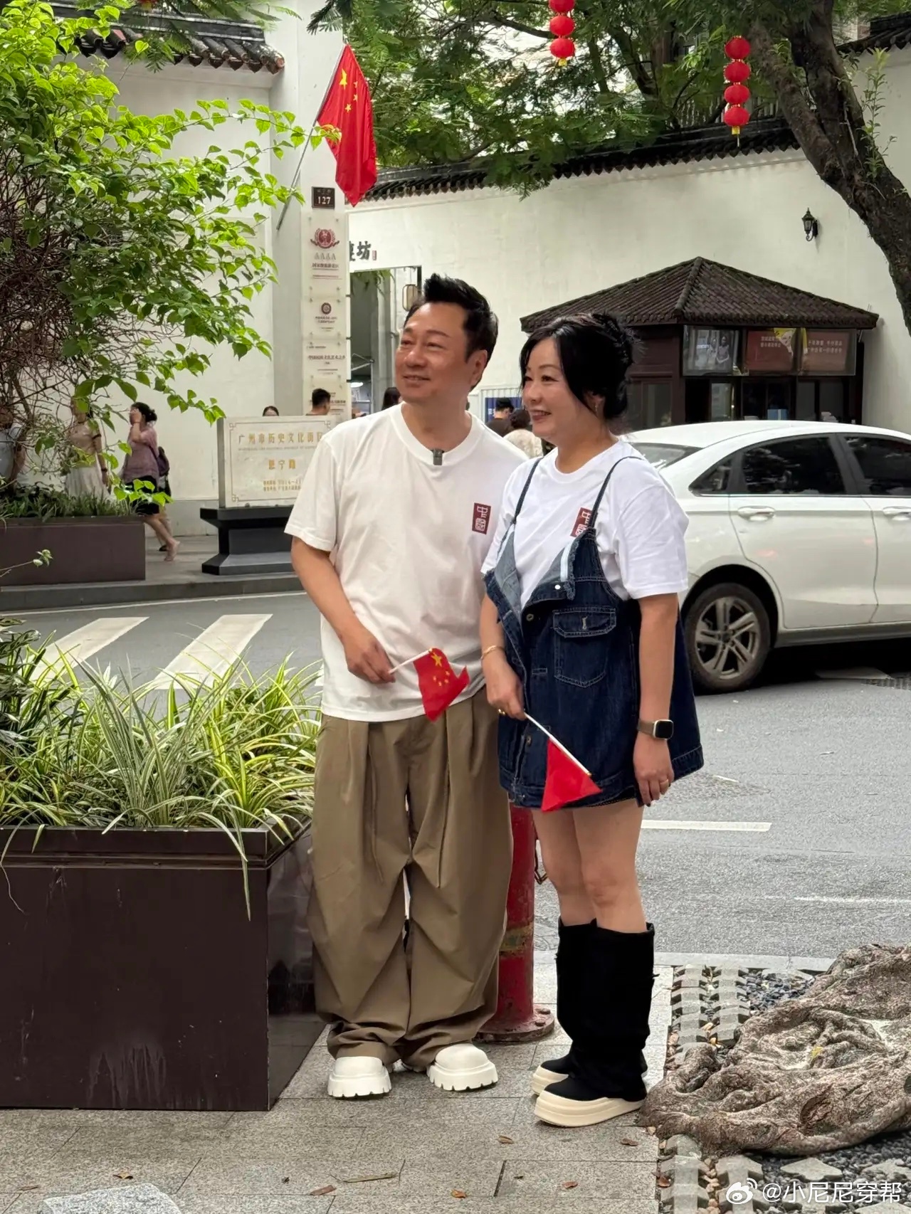 黎耀祥和老婆梁耀莲现身广州永庆坊旅游，两个人站在路边，手里拿着小五星红旗，庆祝即