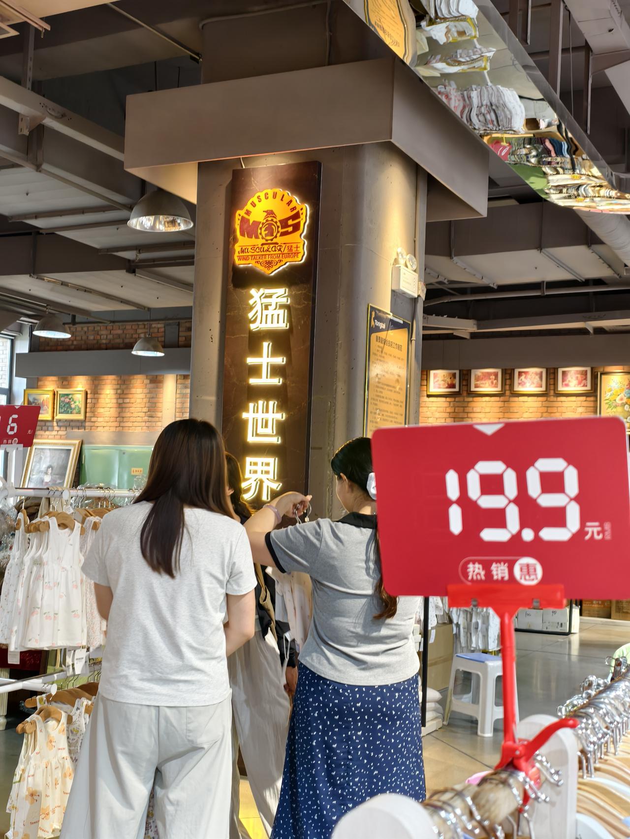 市井生活中的美好的瞬间商超一隅，19.9元热销价牌醒目，顾客驻足挑拣衣饰，日常采