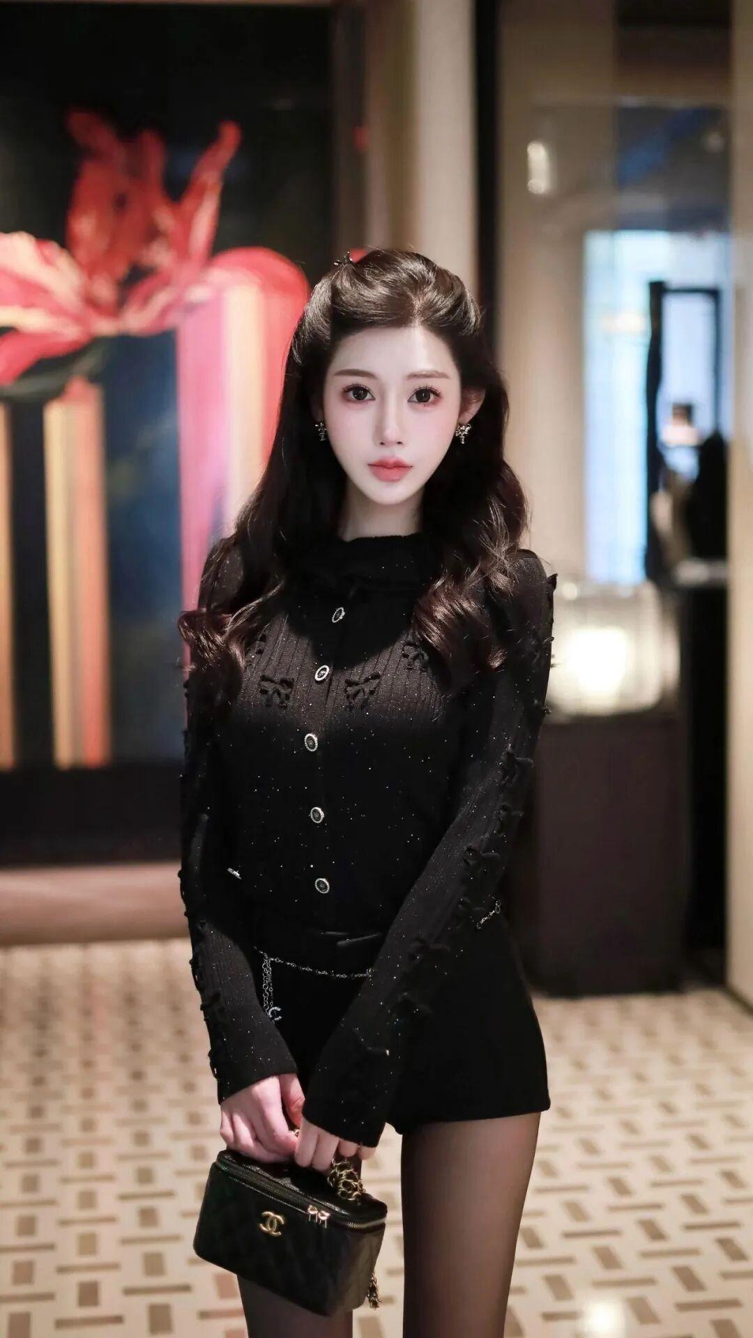 这位美女穿着黑色亮片装，手拿小包，站在画前。紫色亮片裙装 亮片裙装