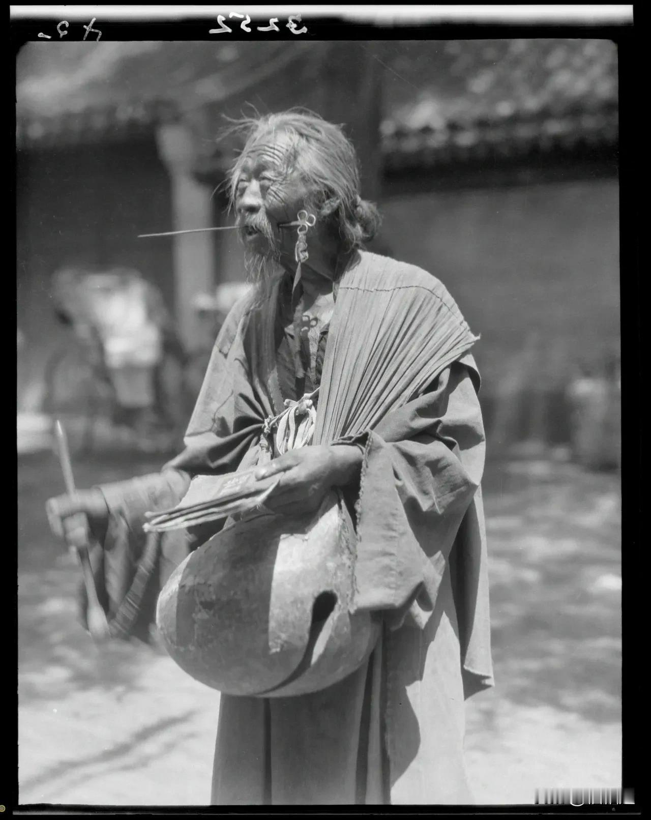 拍摄于1911年的老照片，展示了一位老人在街头卖艺的情景。老人穿着传统的长袍，留