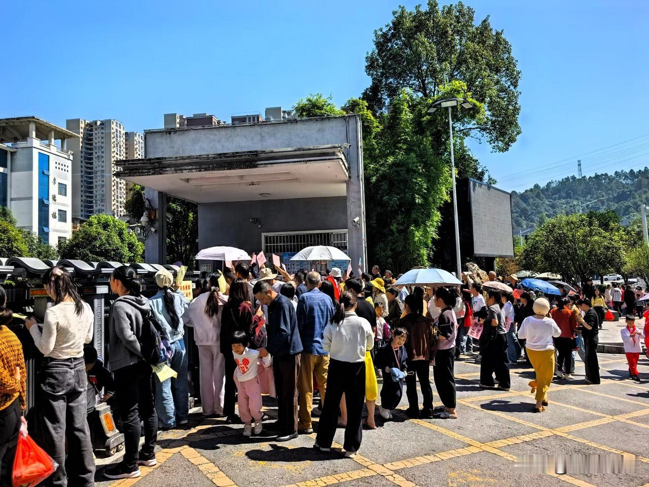 大太阳底下，学校大门外早早挤满了家长。
有人撑着遮阳伞，踮起脚尖往校园里面张望；