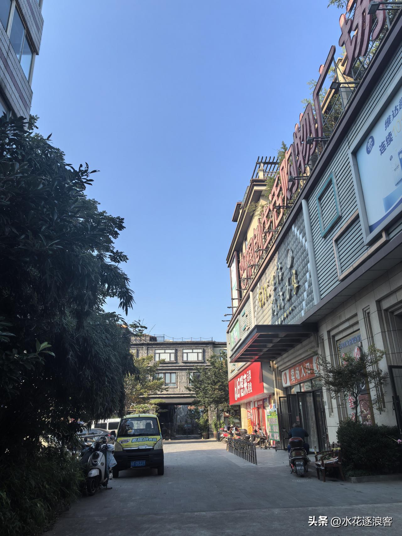 抬头是干净透亮的蓝天，街边商铺安静伫立；小车、电动车停在路旁，满满都是生活烟火气