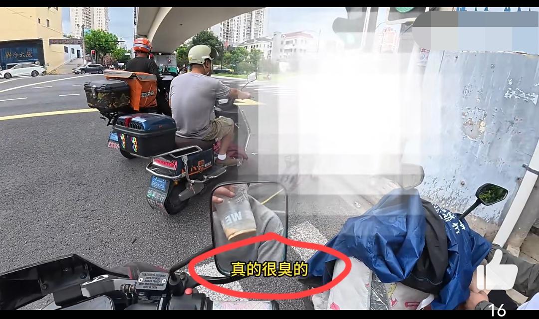 上海街头，路上一名外卖小哥一边骑行一边抽烟。一旁骑自行车的女子闻到烟味，当场进行