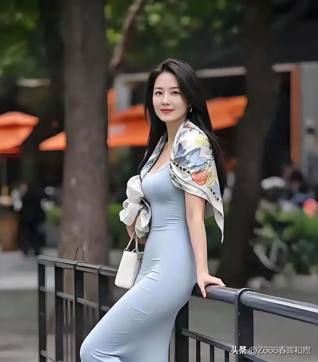 浅蓝裙裾勾勒曼妙身姿，丝巾如彩蝶翩跹肩头。她倚栏浅笑，眸中盛着温柔，街景晕染成画