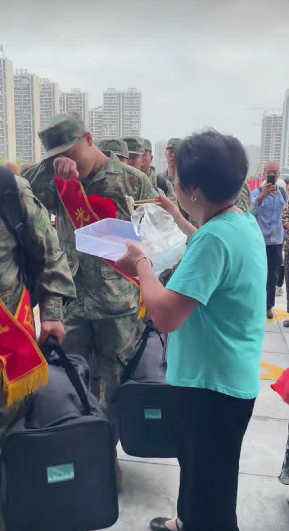 送别新兵入伍现场，一位大娘端着一大盘热呼呼的饺子，喂到一个新兵小伙子的嘴里时，小